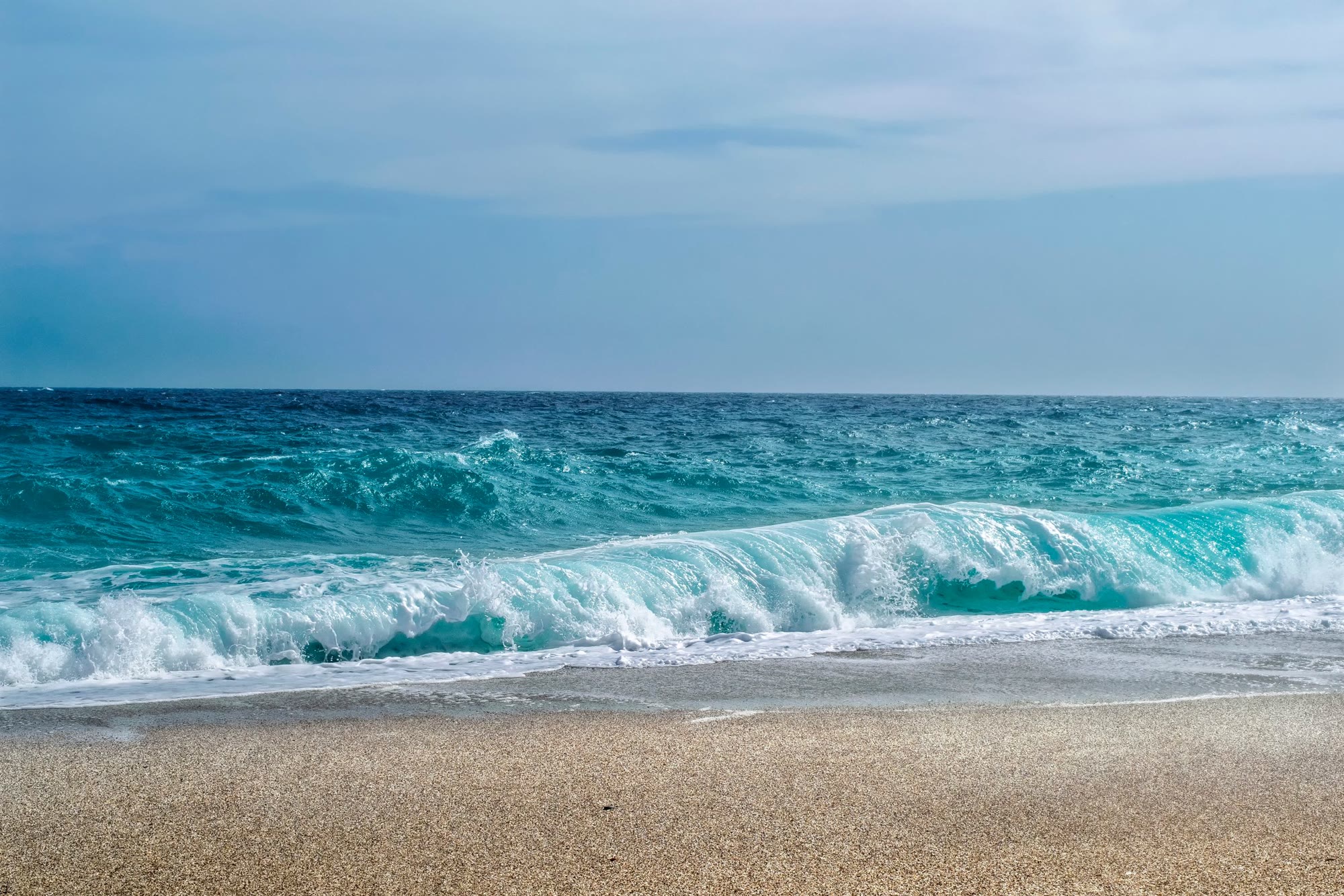 A turquoise wave breaking on a sandy beach, evocative of The Moorings' coastal setting